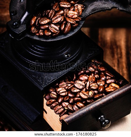 Vintage manual coffee grinder with coffee beans on wooden brown background close up. Coffee Mill with roasted coffee grains.