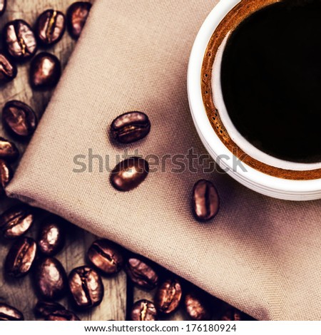 Cup of coffee with coffee beans on  brown napkin on wooden table, closeup. Cup of fresh espresso  on brown background  top view.