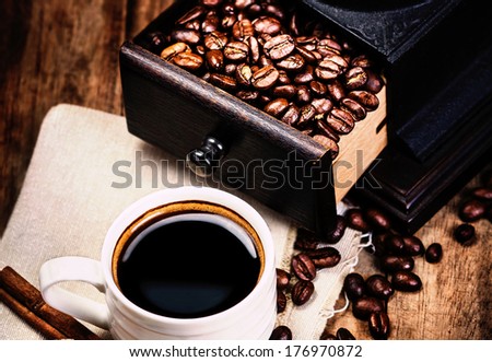 Cup of coffee with coffee beans and Coffee grinder on wooden brown background closeup.  Espresso Cup on brown napkin with cinnamon and sugar.