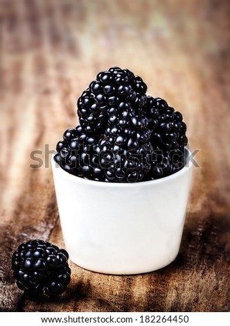 Fresh Blackberries in a white bowl on  wooden table closeup