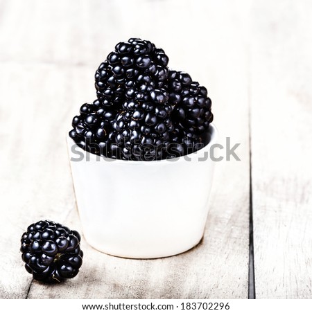 Fresh Blackberries in a white bowl on  wooden background close up in Rustic style.