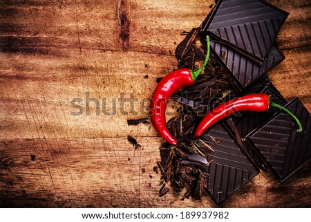 Pieces of Chocolate Bar with Red Chilli Pepper on wooden background closeup. Chunks of Broken dark chocolate bar on wood table macro.