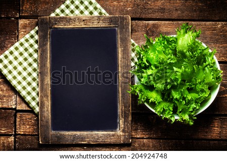 Black chalkboard for menu and fresh salad over wooden background. Diet Food Restaurant and healthy lifestyle concept.