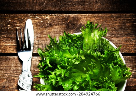 Fresh Salad in a bowl with  measuring tape over wooden table with knife and fork.  Diet Food and healthy lifestyle concept.
