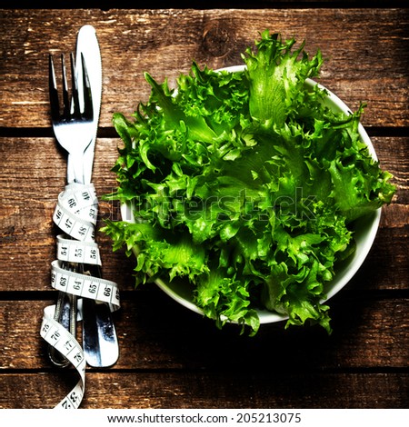 Salad in a bowl with  measuring tape over wooden table with knife and fork.  Diet Food and healthy lifestyle concept.