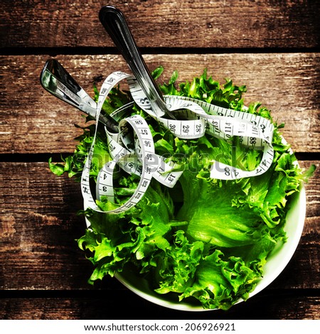 Salad with fitness  measuring tape over wooden background with knife and fork.  Diet Food and healthy lifestyle concept.