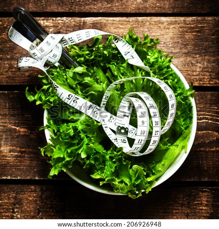 Salad with fitness  measuring tape over wooden background with knife and fork.  Diet Food and healthy lifestyle concept.