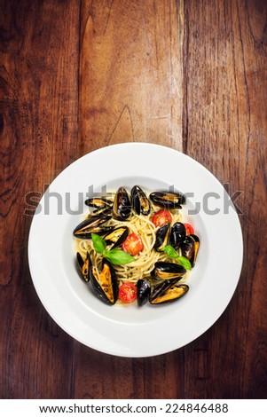 Seafood  Pasta with mussels, cherry tomato  and basil in white plate on wooden table, top view