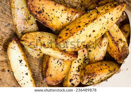 French fries potato wedges in brown craft  paper bag on wooden old background. Fast food. Closeup.