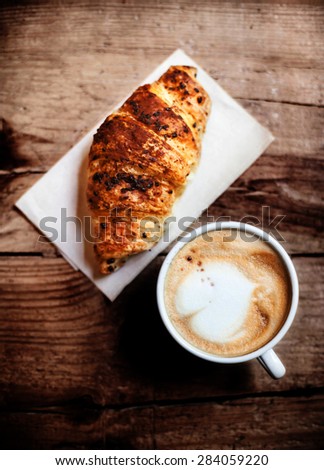 Coffee and fresh croissant for breakfast on rustic wooden table, top view. Chocolate croissant with cappuccino