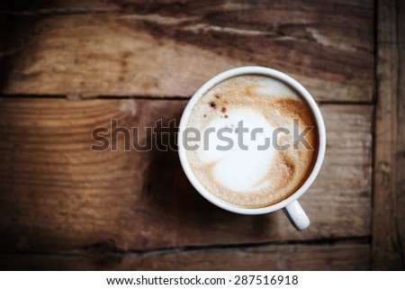 Cup of coffee with heart pattern in a white cup on wooden background. Latte Art, top view.