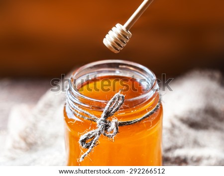 Honey in a glass jar with honey dipper on vintage wooden background close up.
