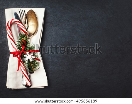 Christmas table place setting with christmas tree branches, spoon, knife, fork and ribbon over black table with copyspace. Christmas holidays background