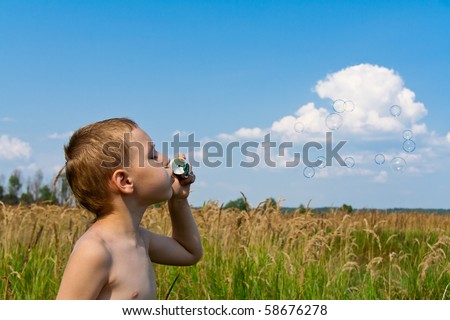Little boy blowing soap bubbles against blue sky