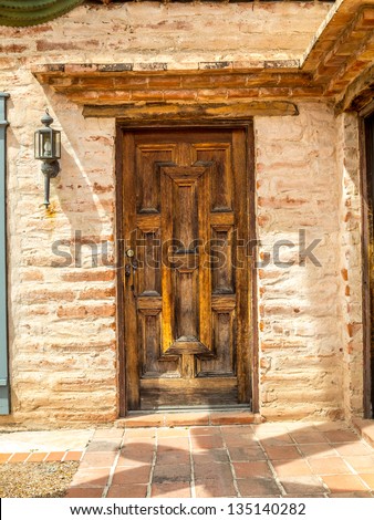Rustic wood door and single exterior light with a cactus shadow in the foreground