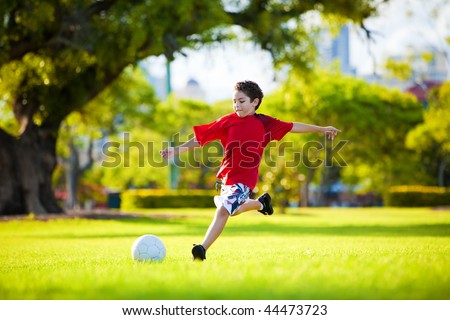 Young excited boy kicking ball in the grass outdoors Young excited boy kicking ball in the grass outdoors