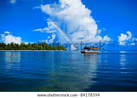 Single boat on the see under the rainbow and tropical island