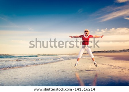 Senior happy woman enjoying beach holiday jumping in air