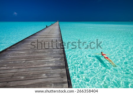 Young woman in red bikini swimming next to jetty in azure water of Maldives