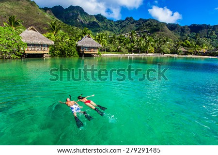 Young couple snorkeling over reef next to resort on a tropical island with over-water villas
