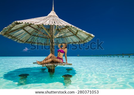 Young beautiful woman in purple bikinis under beach umbrella in the ocean