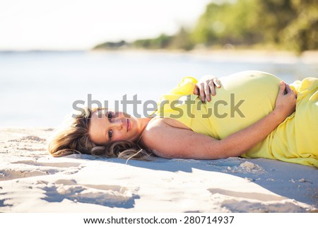 Pregnant woman with long hair in yellow dress lying down on the beach