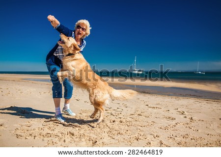 Happy older woman playing on the beach with golden retriever