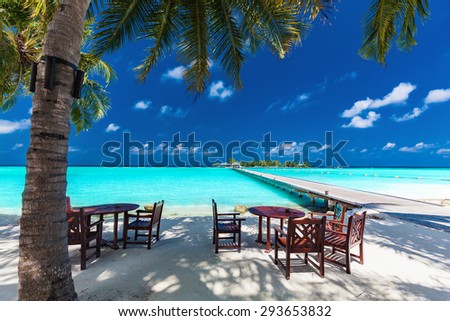 Tables and chairs in the shadow of palm tree on amazing tropical island