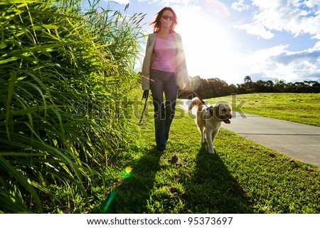 Young woman and golden retriever walking in the grass