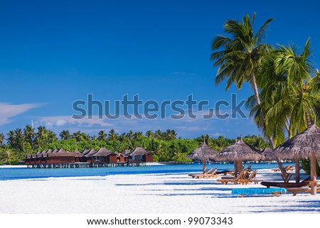 Palm trees and umbrellas over tropical beach with villas over water