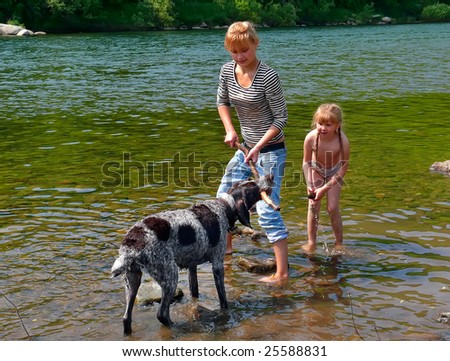 Two young girls play with dog at river.