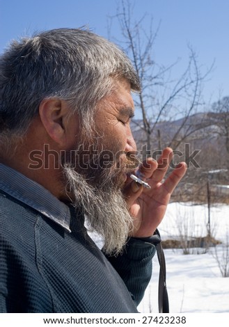 A portrait close up of the old smoking man with grey beard. Small indigenous people of Russian Far East.