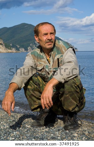 A portrait of the man in camouflage suit, sitting on beach at sea.