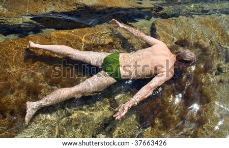 A man swims in water among reefs. View from back. Summer, sunny day.