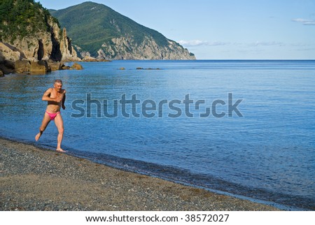 The man runs in water along beach. Summer. Early evening.