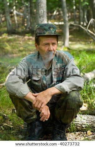 A man in camouflage suit smokes in forest.