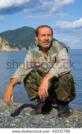 A portrait of the man in camouflage suit, sitting on beach at sea.