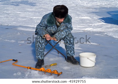 A man on winter fishing on ice of river.