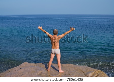 A man sunburns on big flat stone in sea. View from back. On background is blue seawater with surf. Early evening.