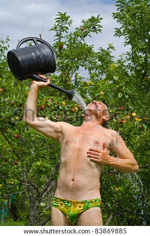 The man waters himself from a watering can in orchard.