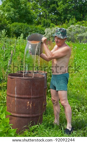 The gardener pours water into a barrel with bucket.