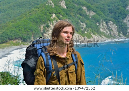 A portrait of the young long-haired man with rucksack at sea.