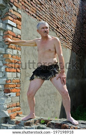 The man in loin-cloth stands at ruins of old building.