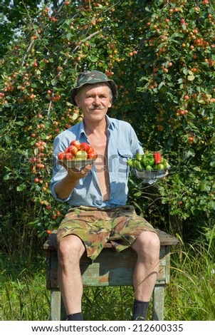 Farmer at apple-tree holds plates with apples and vegetables.