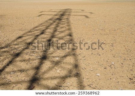 The shadow of a large high voltage electricity pole on the spring field.