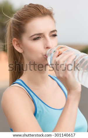 Young woman in sport dress drinks out of a bottle of water