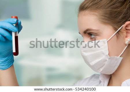 pretty nurse with face mask is holding a blood sample in a laboratory
