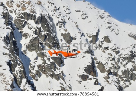 Orange search and rescue chopper flying in front of very steep mountain slope