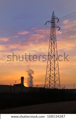Sun will rise behind a smoke column in industrial landscape in winter, with power line, silhouette.
