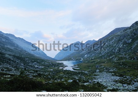 Mountain landscape before dawn (blue hour), with reservoir, meadows, rocks and clouds, cold cast
